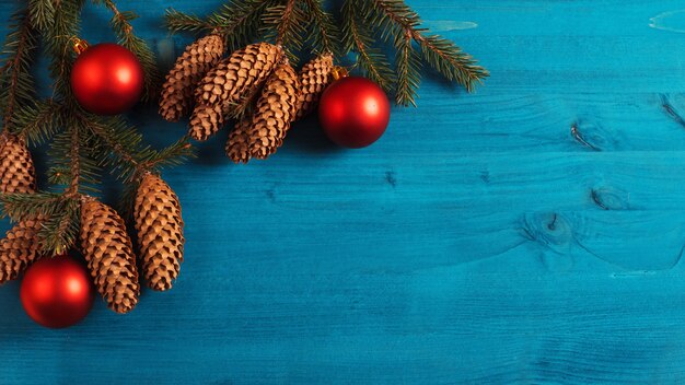 Vista dall'alto dello sfondo di Natale, rami di un albero di Natale con coni su uno sfondo di legno blu. Palline rosse, copia spazio