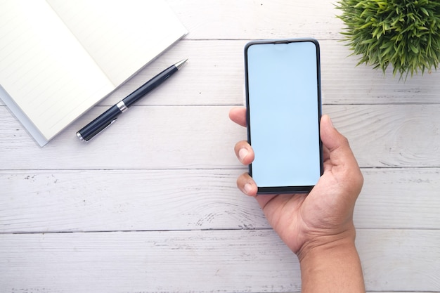 Vista dall'alto dello smartphone che tiene la mano dell'uomo con lo schermo vuoto sulla scrivania dell'ufficio