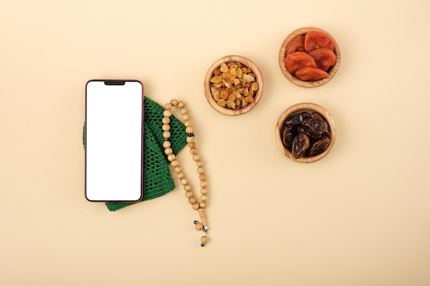 Vista dall'alto dello smartphone con rosario a schermo bianco che giace accanto alla frutta secca concetto religioso amore per l'Islam copia spazio mock up