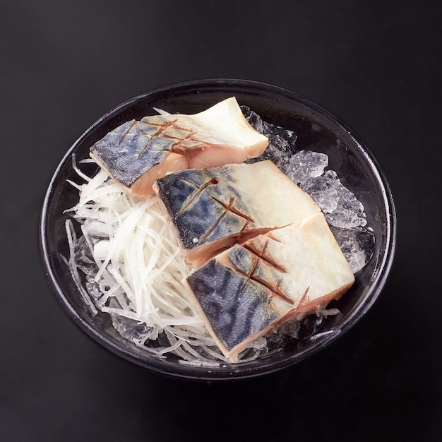 Vista dall'alto di 3 shime sashimi saba a fette e ravanello a fette posto sul ghiaccio in una ciotola nera isolata su sfondo nero