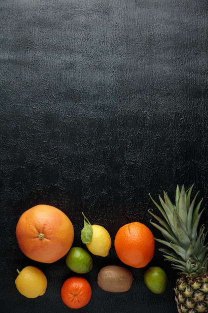 Vista dall'alto di agrumi come ananas lime kiwi limone arancione su sfondo nero con spazio per la copia