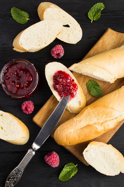 Vista dall'alto di baguette francese e marmellata di lamponi fatta in casa su fondo di legno nero