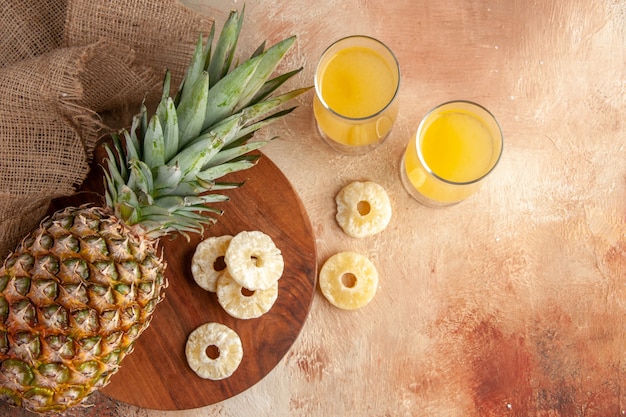 Vista dall'alto di bicchieri di succo di ananas fresco fette di ananas secche su tavola di legno su sfondo beige