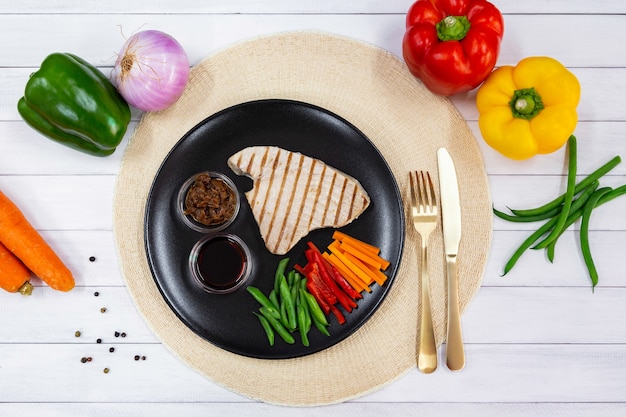 Vista dall'alto di bistecca di tonno alla griglia su piastra nera con salsa, cipolla caramellata e verdure fresche