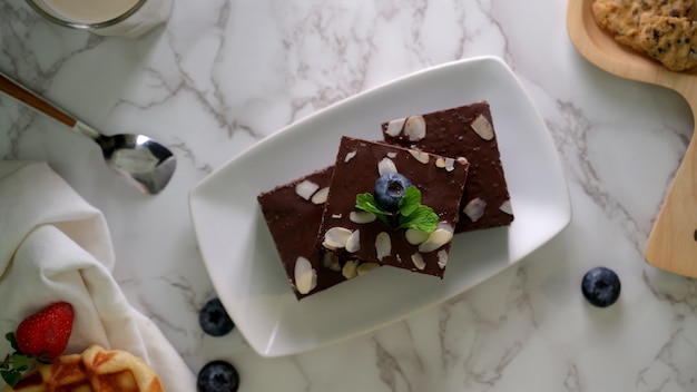 Vista dall'alto di brownies al cioccolato sul piatto bianco con e mirtilli decorati sul tavolo di marmo