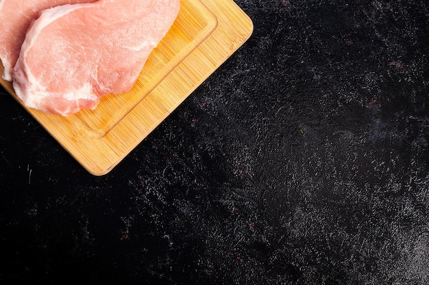 Vista dall'alto di carne cruda fresca su tavola di legno su fondo di legno nero. Cibo gourmet e pasto fresco crudo