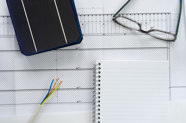 Vista dall'alto di celle solari, blocco note, occhiali e cavo elettrico come concetto di pianificazione per il progetto fotovoltaico