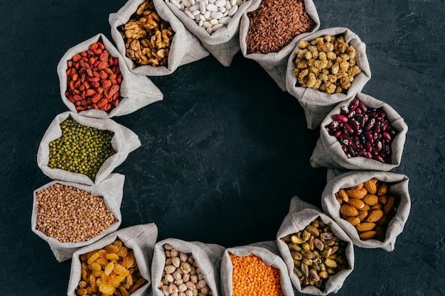 Vista dall'alto di cereali nutrienti colorati e frutta secca in piccoli sacchi in piedi in cerchio isolati su sfondo scuro Concetto di cibo