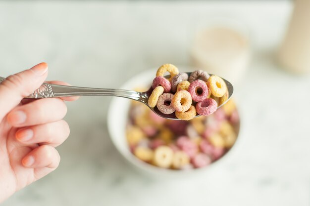 Vista dall'alto di cereali per la colazione colorati luminosi in una ciotola con cucchiaio su sfondo bianco