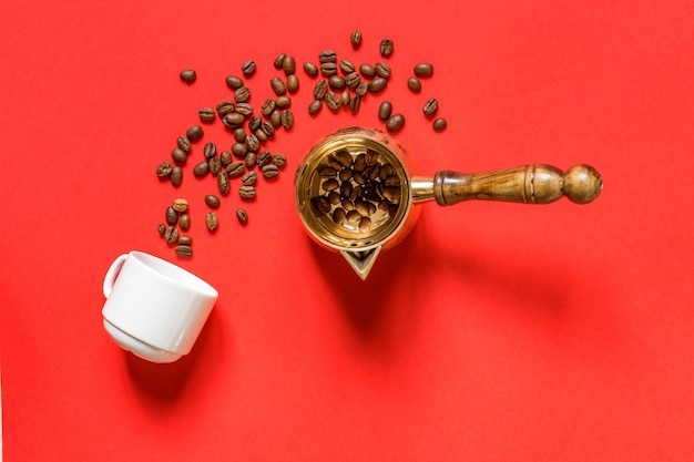 Vista dall&#39;alto di chicchi di caffè in cezve (tradizionale caffettiera turca), tazza di whte su sfondo rosso.