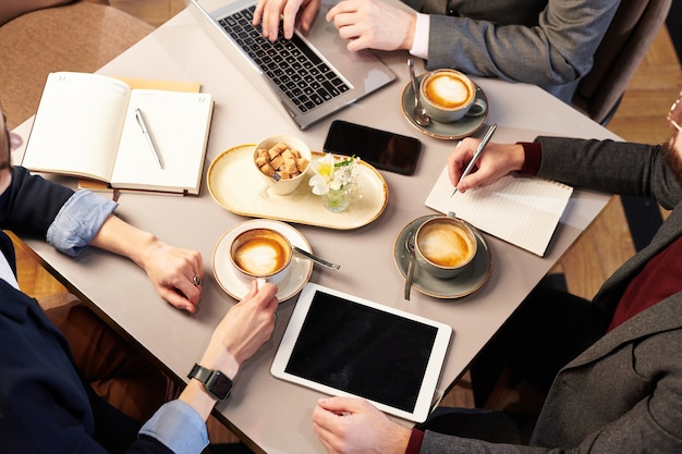 vista dall'alto di colleghi di lavoro irriconoscibili seduti alla scrivania e bere cappuccino piagnucolare pranzando insieme nel ristorante