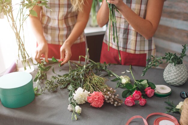 Vista dall'alto di consegna fiori. Fioristi che creano ordine, realizzano bouquet di rose nel negozio di fiori. Due fioriste femminili stanno facendo mazzi di fiori. Una donna che raccoglie rose per un mazzo, anche un'altra ragazza lavora.