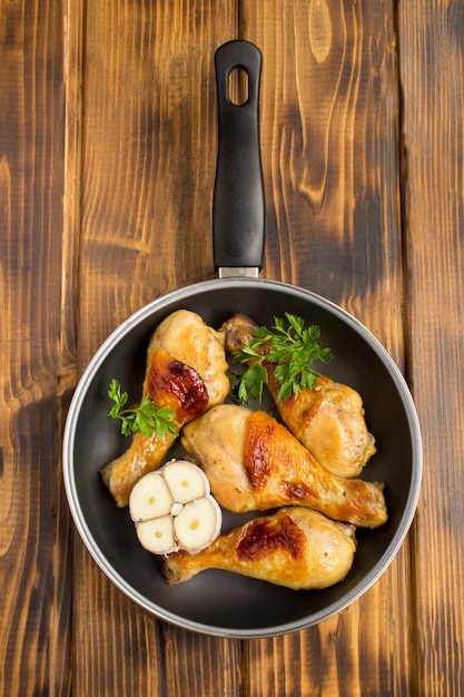 Vista dall'alto di cosce di pollo fritte in padella sul tavolo di legno.