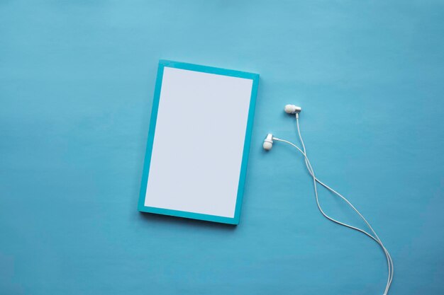 Vista dall'alto di cuffie e notebook bianchi su sfondo blu con spazio per la copia Audiolibro piatto