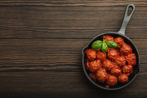 Vista dall'alto di deliziose polpette con salsa di pomodoro e basilico fresco in padella rustica vintage in ghisa servita su fondo di legno. Gustose polpette fatte in casa con spazio per il testo