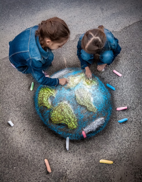 Vista dall'alto di due ragazze che disegnano un'immagine realistica della Terra con i gessi sul terreno on