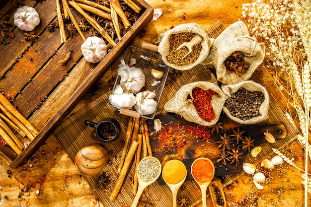 Vista dall&#39;alto di erbe aromatiche, peperoncino piccante, peperoncino in polvere in cucchiai, aglio, spezie in sacchi, cannella,