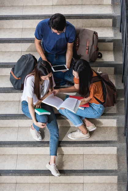 Vista dall'alto di felici giovani studenti asiatici e studentesse mostrano i loro libri ai loro amici all'università, Istruzione torna al concetto universitario