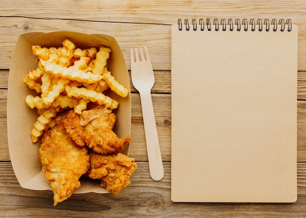 Vista dall'alto di fish and chips con forchetta e taccuino