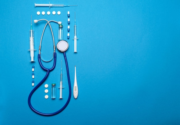 Vista dall'alto di forniture mediche - stetoscopio, pillole, siringhe, termometro e fiala di vaccino su sfondo blu