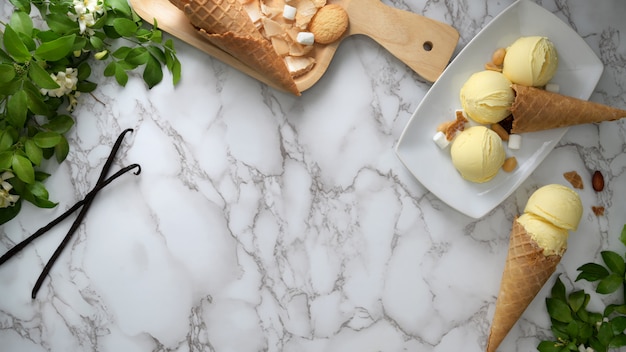 Vista dall'alto di gelato alla vaniglia con coni, topping e copia spazio sulla scrivania di marmo