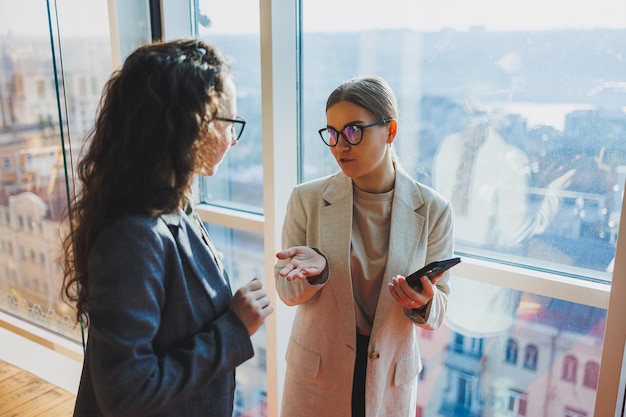 Vista dall'alto di giovani lavoratori d'affari fiduciosi sorridenti in abiti casual in piedi sullo sfondo dell'ufficio moderno e che parlano durante la pausa del giorno