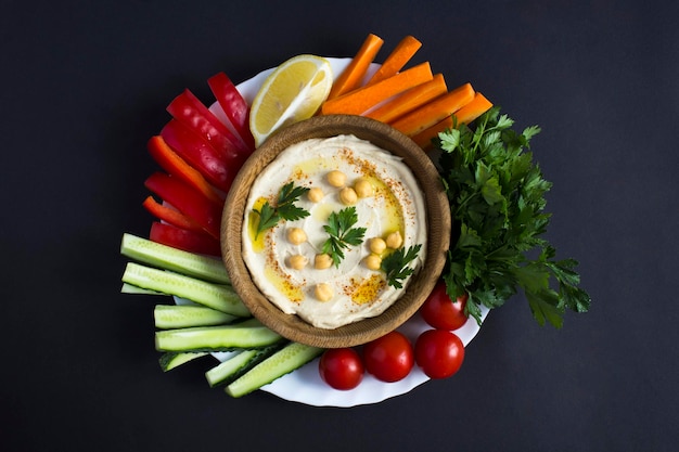 Vista dall'alto di hummus nella ciotola e verdura su sfondo nero Primo piano