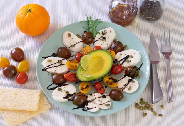 Vista dall'alto di insalata caprese. Un piatto con mozzarella di formaggio e pomodorini, pepe e balsamico. Mezzo avocado e un'arancia per completare un pasto sano