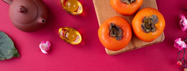 Vista dall'alto di kaki di cachi dolci freschi con foglie su sfondo rosso da tavola per il concetto di design di frutta del capodanno lunare cinese, la parola significa che la primavera sta arrivando.