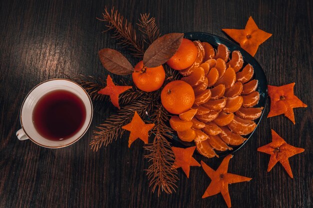 Vista dall'alto di mandarini con foglie in decorazioni natalizie con albero di Natale, arancia essiccata e bacche su un vecchio tavolo di legno. Stile rustico scuro