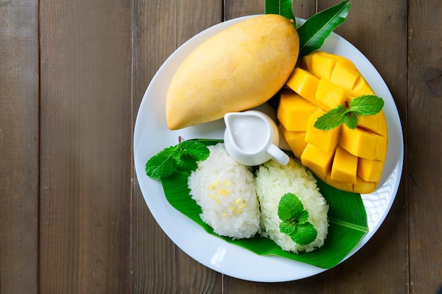 Vista dall'alto di mango maturo con riso appiccicoso aromatizzato al cocco su piatto di legno