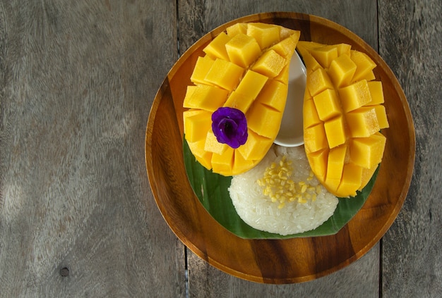 Vista dall'alto di mango maturo fresco e riso appiccicoso con latte di cocco su legno