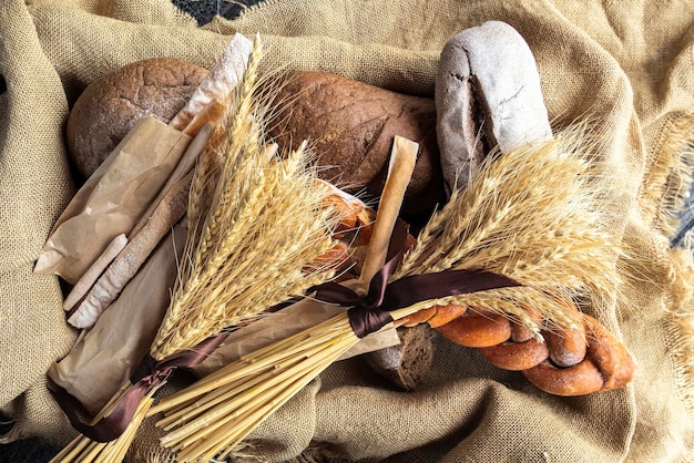 Vista dall'alto di pane fresco e altri prodotti da forno in un cesto rivestito di tela e spighe di segale e grano