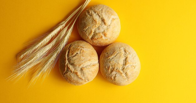 Vista dall'alto di panini rotondi disposti di pane dorato croccante su sfondo giallo con spighe di grano