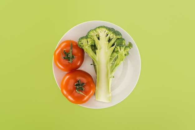 Vista dall'alto di pomodori rossi vicino a broccoli biologici su piatto bianco isolato su verde