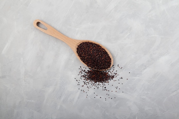 Vista dall'alto di quinoa nera organica in cucchiaio di legno su sfondo grigio