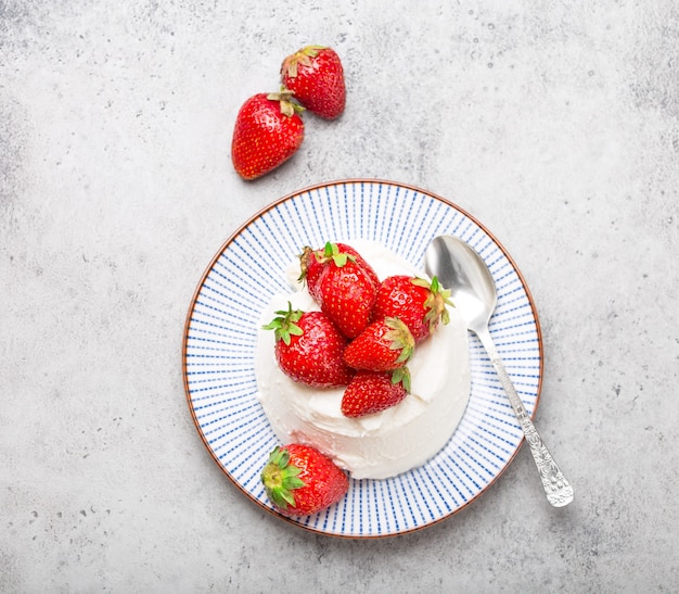 Vista dall'alto di ricotta di formaggio italiano fresco con fragole su un piatto con un cucchiaio, sfondo grigio pietra rustica