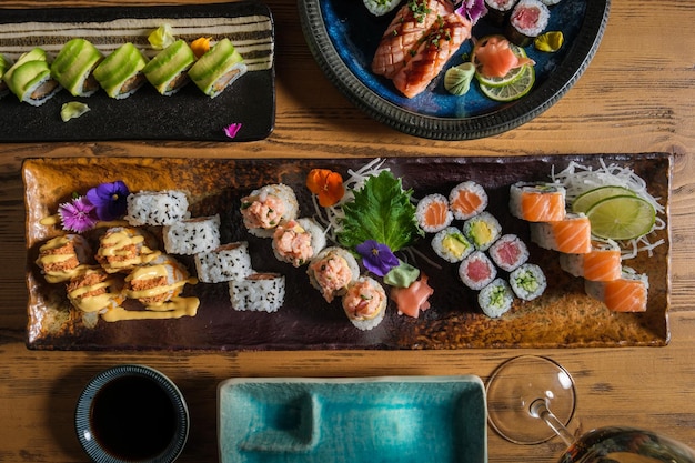 Vista dall'alto di rotoli di sushi freschi assortiti serviti su vassoi su un tavolo di legno con bicchiere di vino e salsa di soia in un caffè