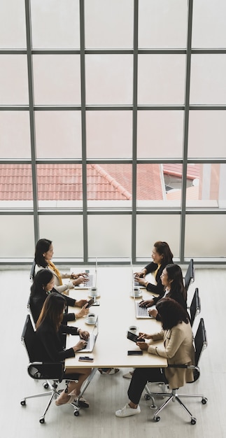 Vista dall'alto di sei donne d'affari dirigenti sedute su ciascuna sedia utilizzando computer portatili e tablet sul tavolo da conferenza in legno nella sala riunioni in ufficio. Concetto per incontro di lavoro.