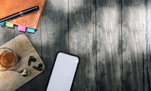 Vista dall'alto di smartphone con schermo vuoto, tazza di caffè, notebook e gadget su sfondo di legno.