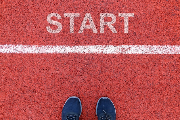 Vista dall&#39;alto di sneakers umane in piedi sulla pista rossa dietro la linea di partenza, con successo