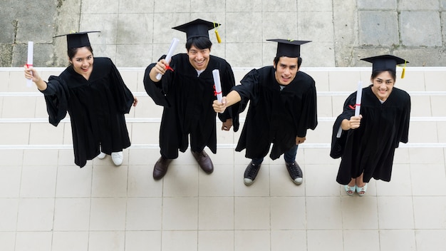 Vista dall&#39;alto di studenti con gli abiti da laurea e cappello stand e tenere il diploma.