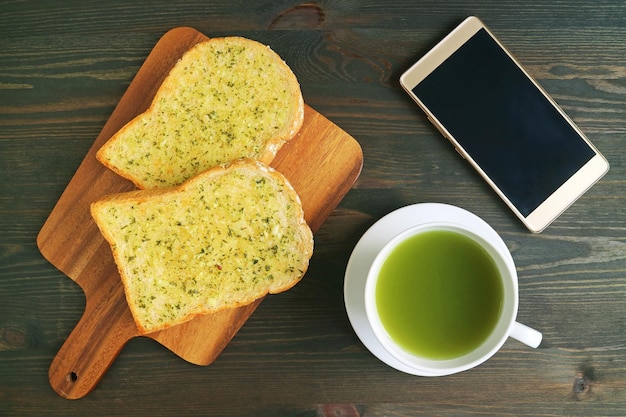 Vista dall'alto di toast al burro all'aglio con tè verde caldo e smartphone con schermo vuoto