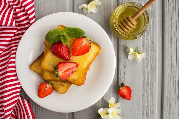 Vista dall'alto di toast francesi con fragole e miele nel piatto bianco sulla superficie grigia