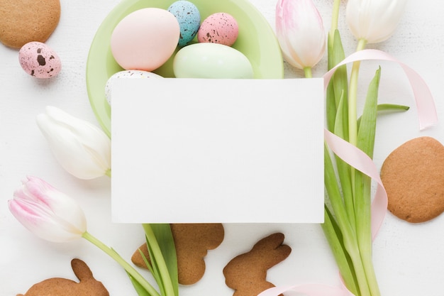 Vista dall'alto di tulipani e uova di Pasqua colorate con pezzo di carta in cima