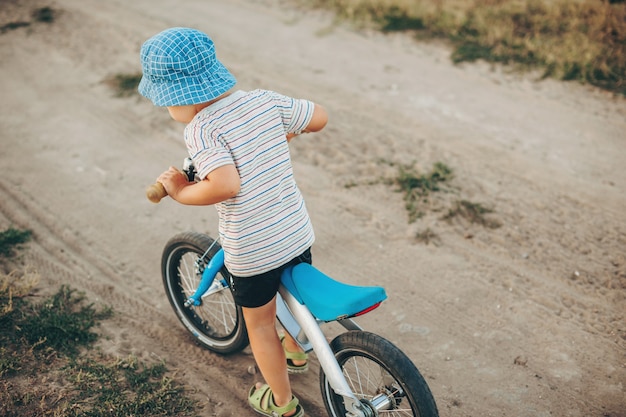 Vista dall'alto di un bambino in bicicletta su una strada di campagna che si gode la vista posteriore del cappello blu del tempo libero