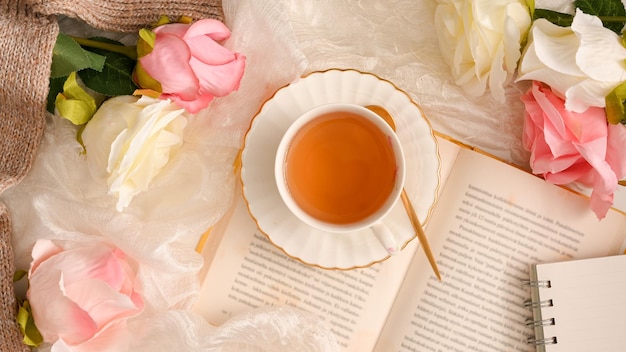 Vista dall'alto di un bellissimo spazio di lavoro femminile con una tazza da tè del romanzo e decorazioni di fiori di rose