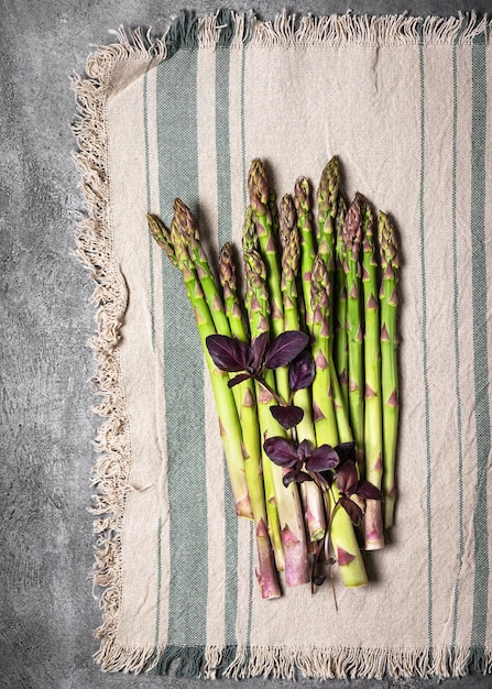 Vista dall'alto di un fascio di asparagi verdi freschi con foglie di basilico viola su una tovaglia di linea rustica