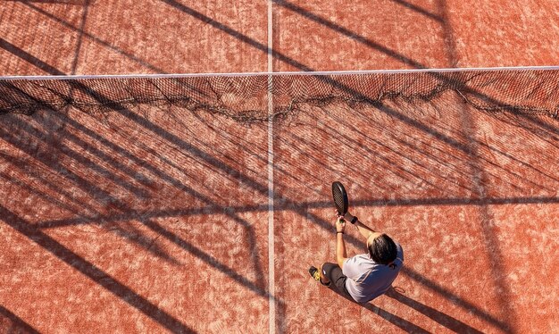 Vista dall'alto di un giocatore di paddle tennis in piedi vicino alla rete con la racchetta su un campo all'aperto.