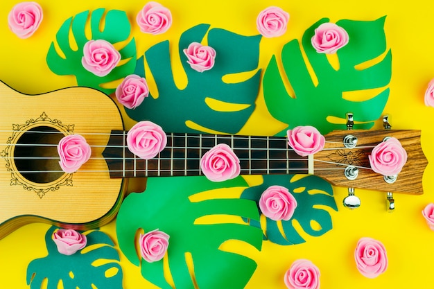 Vista dall'alto di un modello di fiori rosa e chitarra su sfondo giallo vibrante